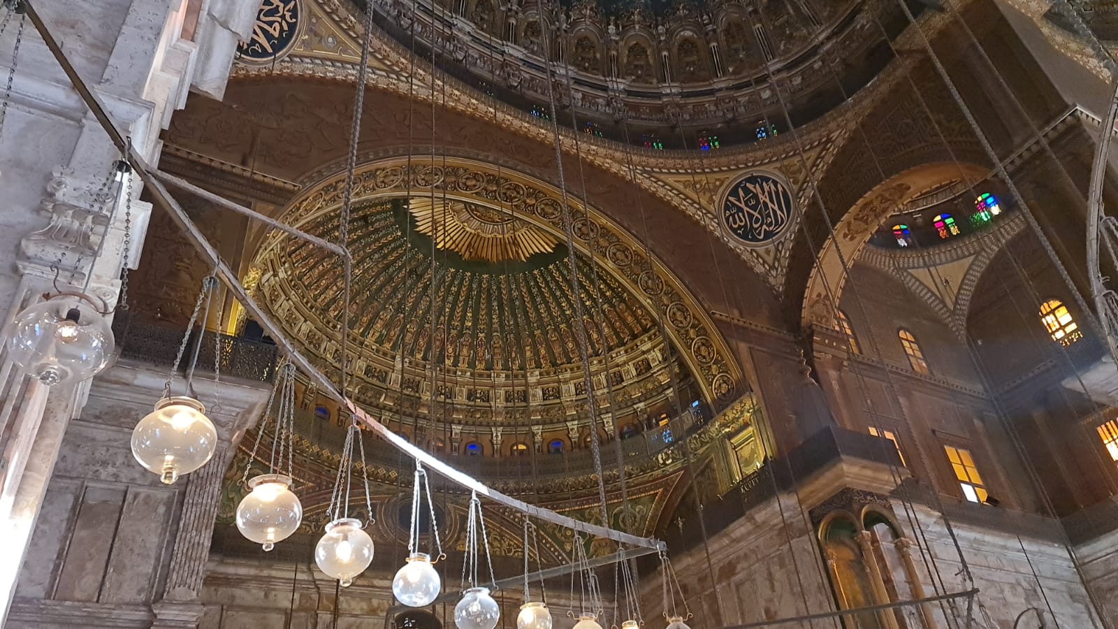 Ornate gilded interior dome of the Muhammad Ali Mosque with hanging glass lamps